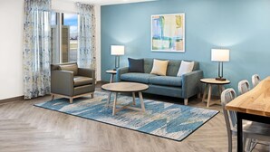 A modern living room with a blue wall, a grey sofa, a wooden coffee table, and a dining table with chairs. - Woodspring Suites Billings (Billings)