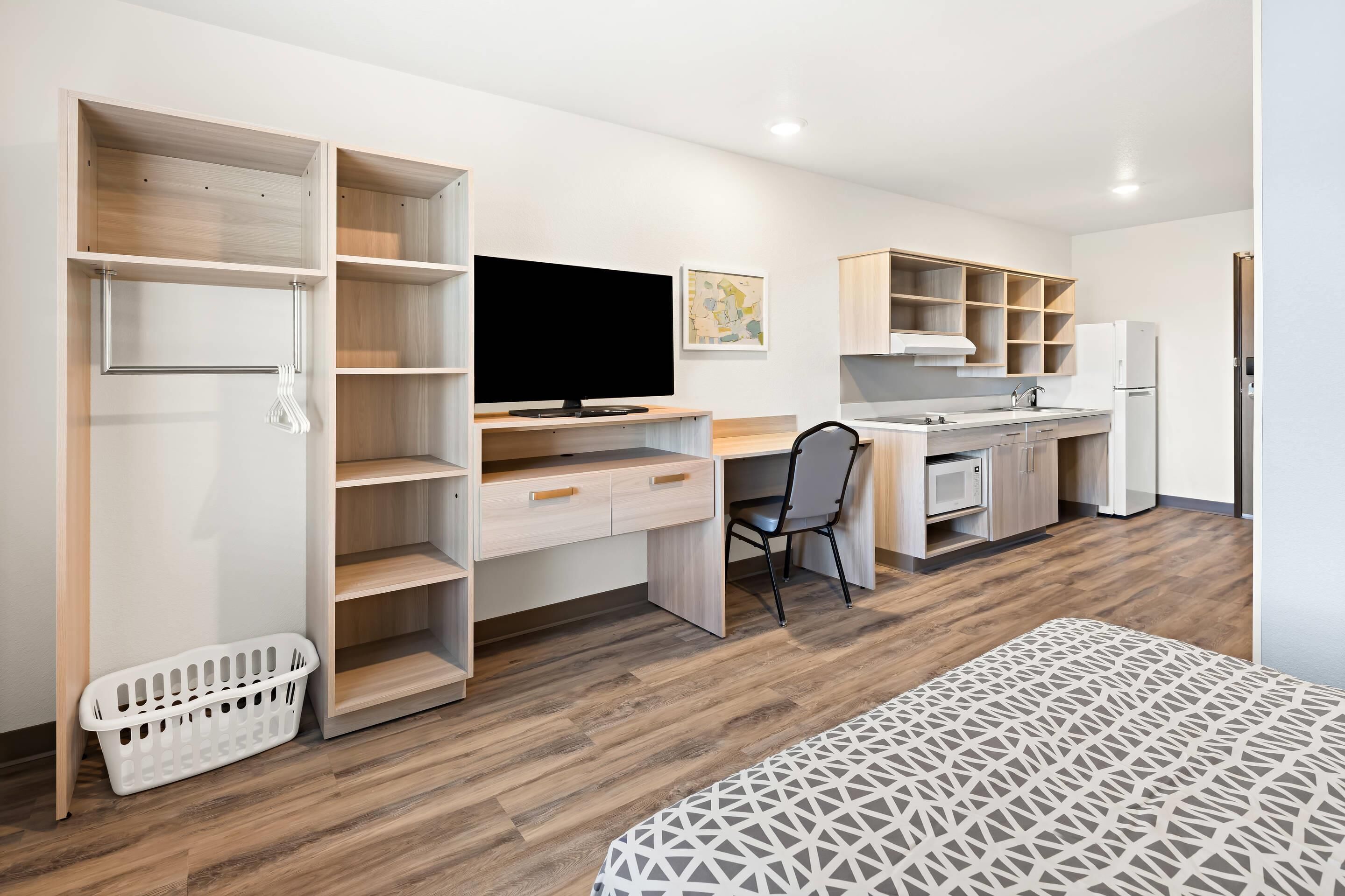 A modern, open-plan bedroom and kitchen with a large wardrobe, a flat-screen TV, a desk, and a dining area.