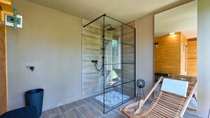 Een moderne badkamer met een douchecabine van glas, een houten bankje en een klein krukje.