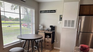 A kitchen with a round table, two stools, a coffee station, and a stainless steel refrigerator.
