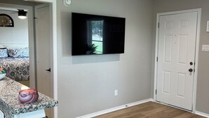 A kitchen with a granite countertop, a bar stool, a television mounted on the wall, and a patterned rug on the floor.