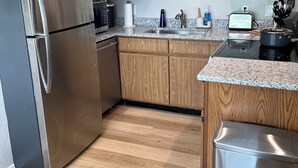 A modern kitchen with wooden cabinets, stainless steel appliances, granite countertops, and a stainless steel trash can.