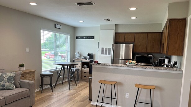 A modern kitchen with wooden cabinets, a stainless steel refrigerator, and a bar area with stools.