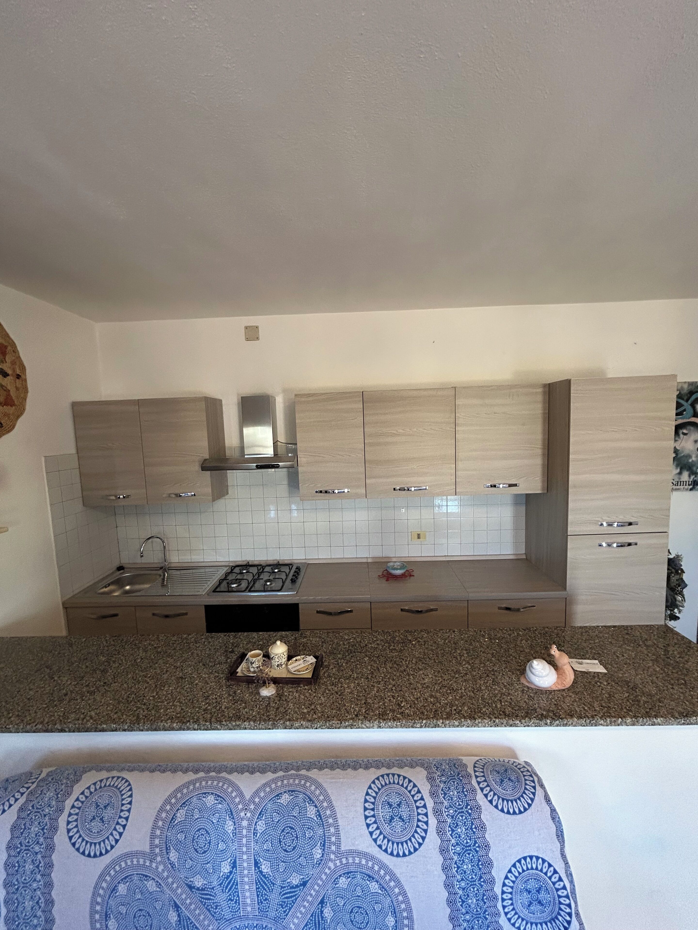 A modern kitchen with light wood cabinets, a stainless steel range hood, and a granite countertop.
