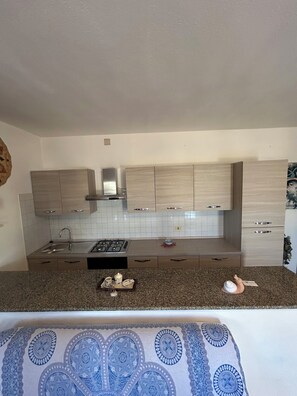 A modern kitchen with light wood cabinets, a stainless steel range hood, and a granite countertop.