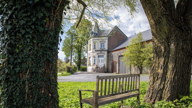 A bench in a grassy area with a building in the background. - Villa BeauSejour in the heart of the countryside  (Baives)