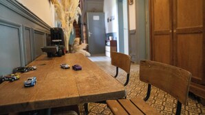 A wooden dining table with toy cars, a chair, and a vase of dried plants in a hallway with patterned flooring and a wooden door. - Villa BeauSejour in the heart of the countryside  (Baives)