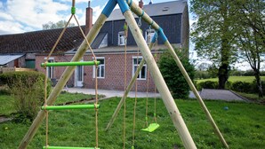 A wooden swing set in a grassy yard with a brick house in the background. - Villa BeauSejour in the heart of the countryside  (Baives)