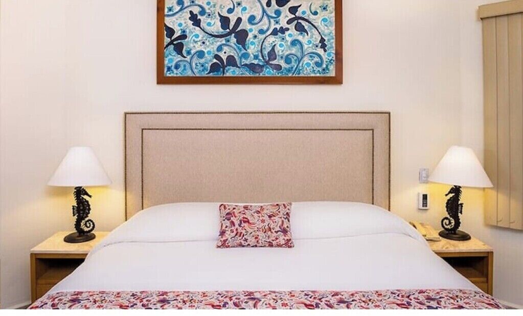 Ett hotellrum med en stor säng, två sängbord med lampor, en dekorativ prydnadskudde och ett inramat konstverk på väggen.