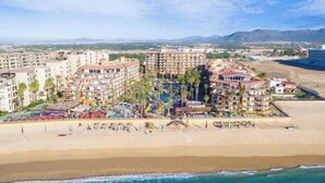 Un hôtel situé sur la côte, composé de plusieurs bâtiments, avec une plage et un paysage montagneux en arrière-plan.