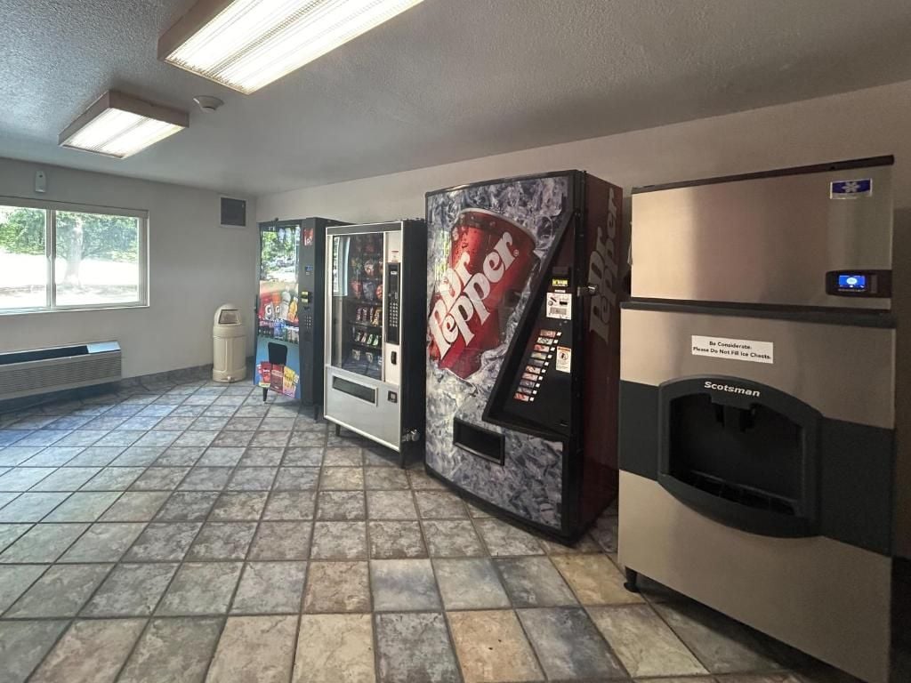 Uma área de máquinas de venda automática com Dr Pepper e Scotman, uma lata de lixo e uma janela com vista para árvores.