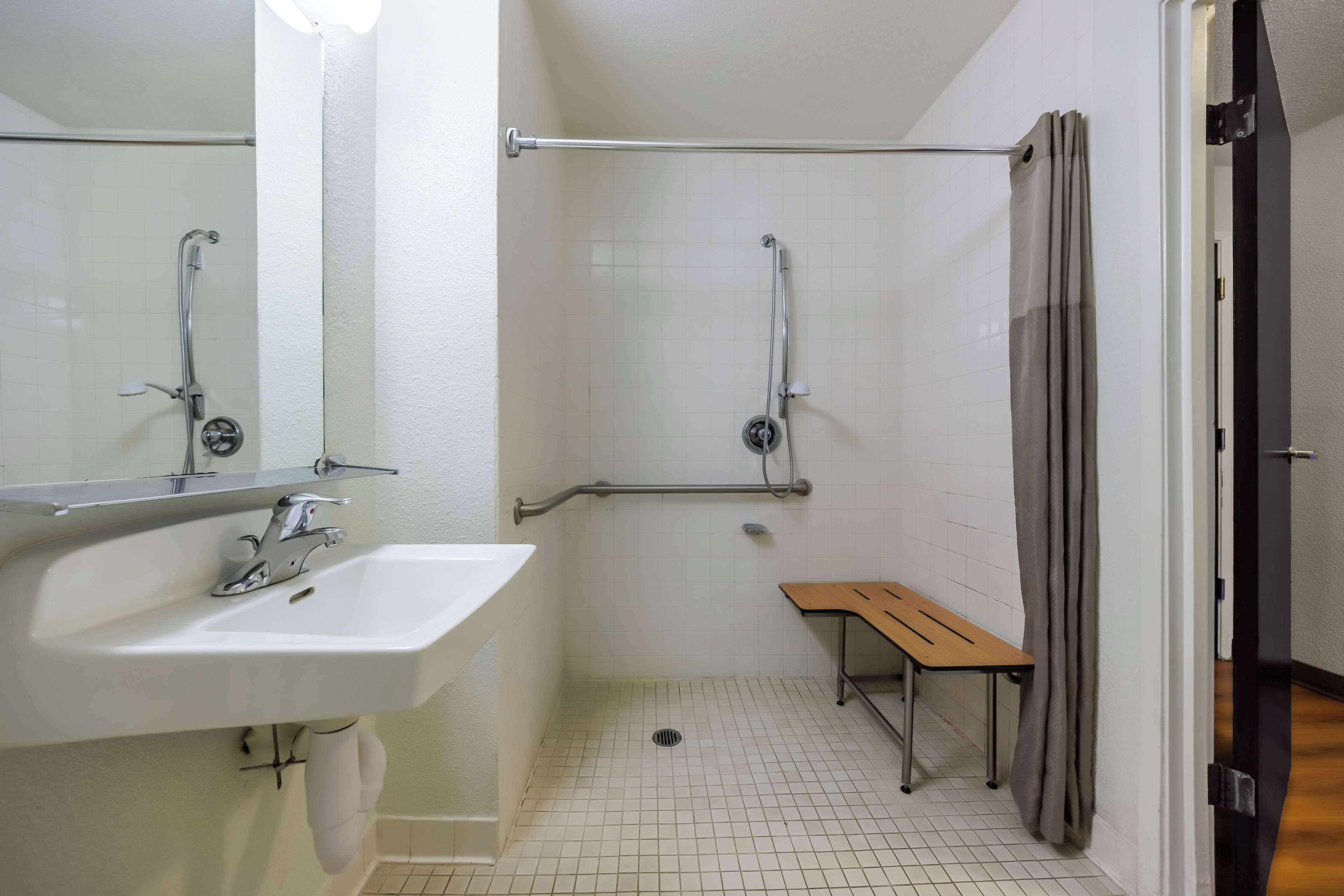 A bathroom with a white sink, mirror, and shower with grab bars.
