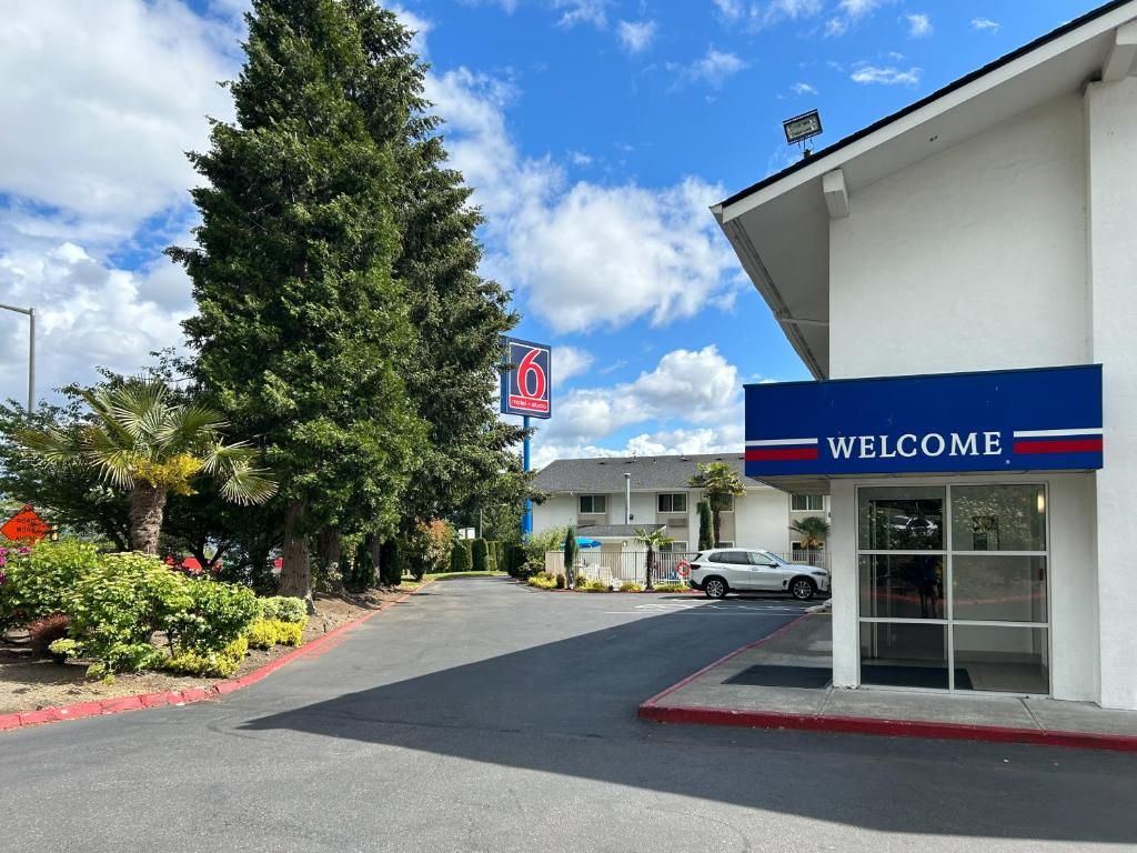 A hotel entrance with a 'WELCOME' sign, a parking lot, and a '6' sign indicating the hotel number.