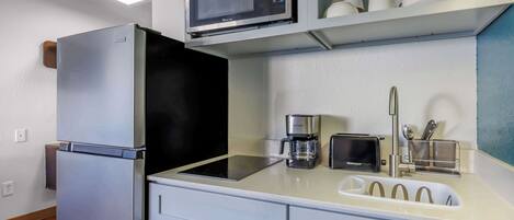 A compact kitchen with a refrigerator, microwave, toaster, coffee maker, and a sink with a faucet.