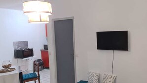 Een knus woongedeelte met een eethoek, een magnetron, een kleine koelkast en een aan de muur bevestigde televisie.