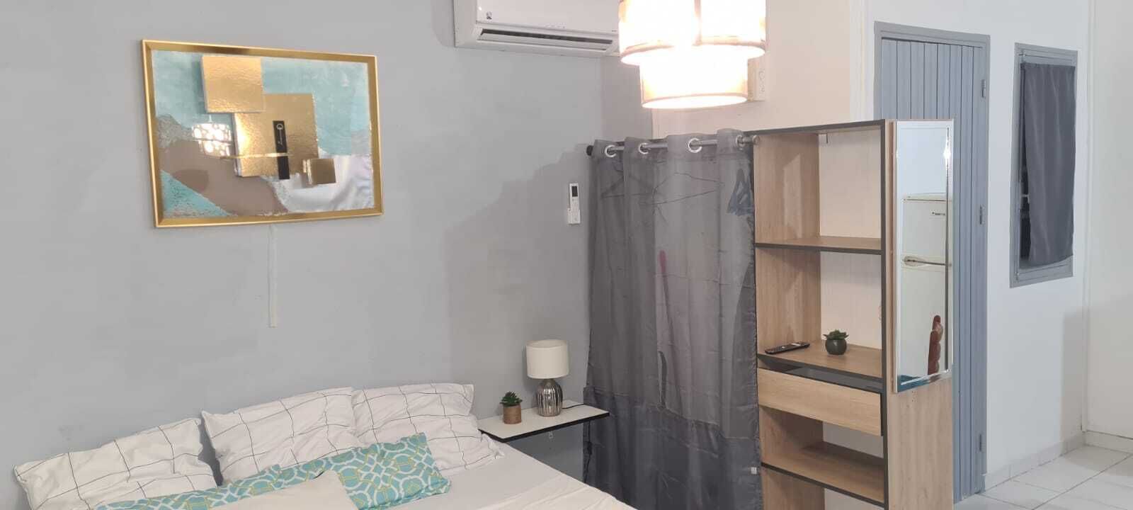 Een slaapkamer met een bed, een nachtkastje met een lamp, een spiegel en een wandairconditioner.