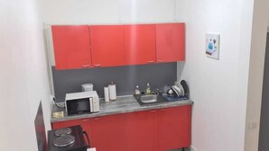 Een kleine keuken met rode kastjes, een magnetron, een spoelbak en een afdruiprek.