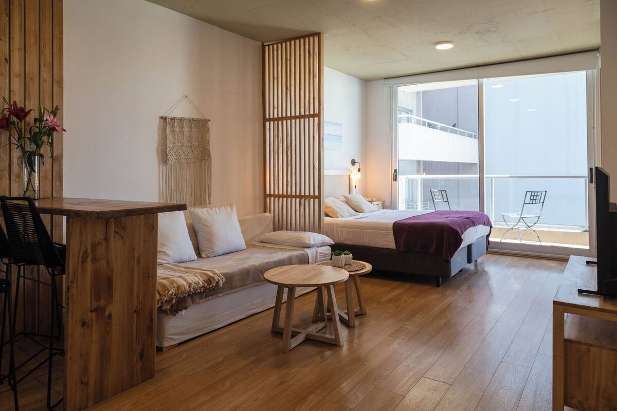 Une chambre moderne avec un plancher en bois, un canapé, un lit, une petite table et un téléviseur.