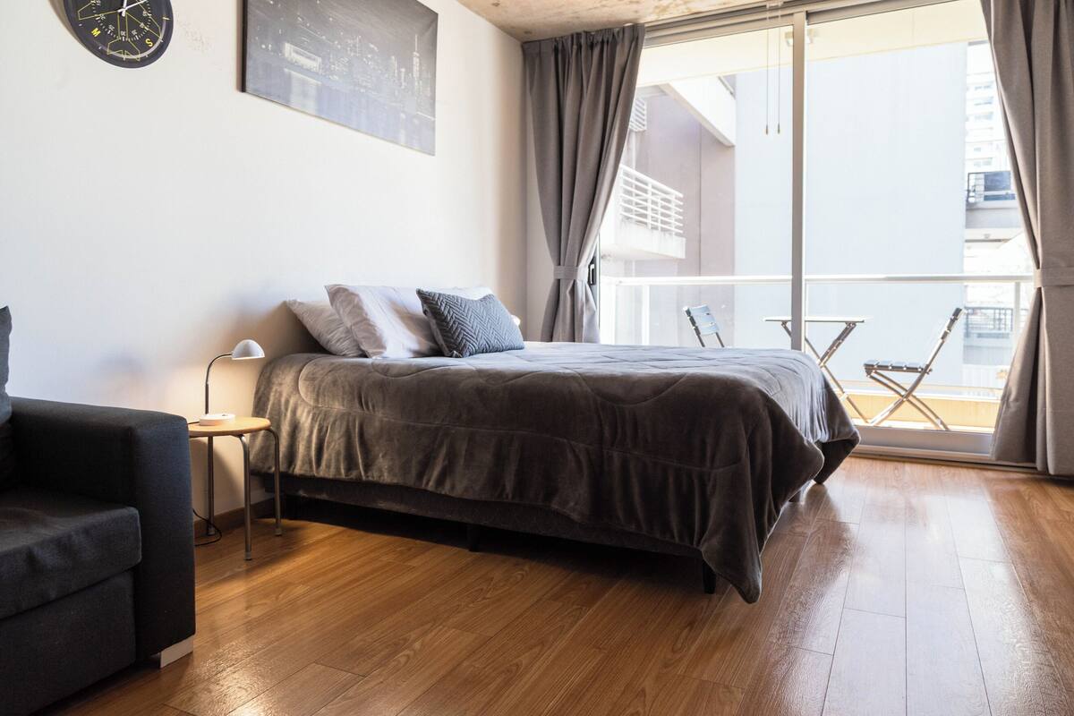 Une chambre à coucher avec un lit, une chaise, un bureau et une fenêtre avec des rideaux.