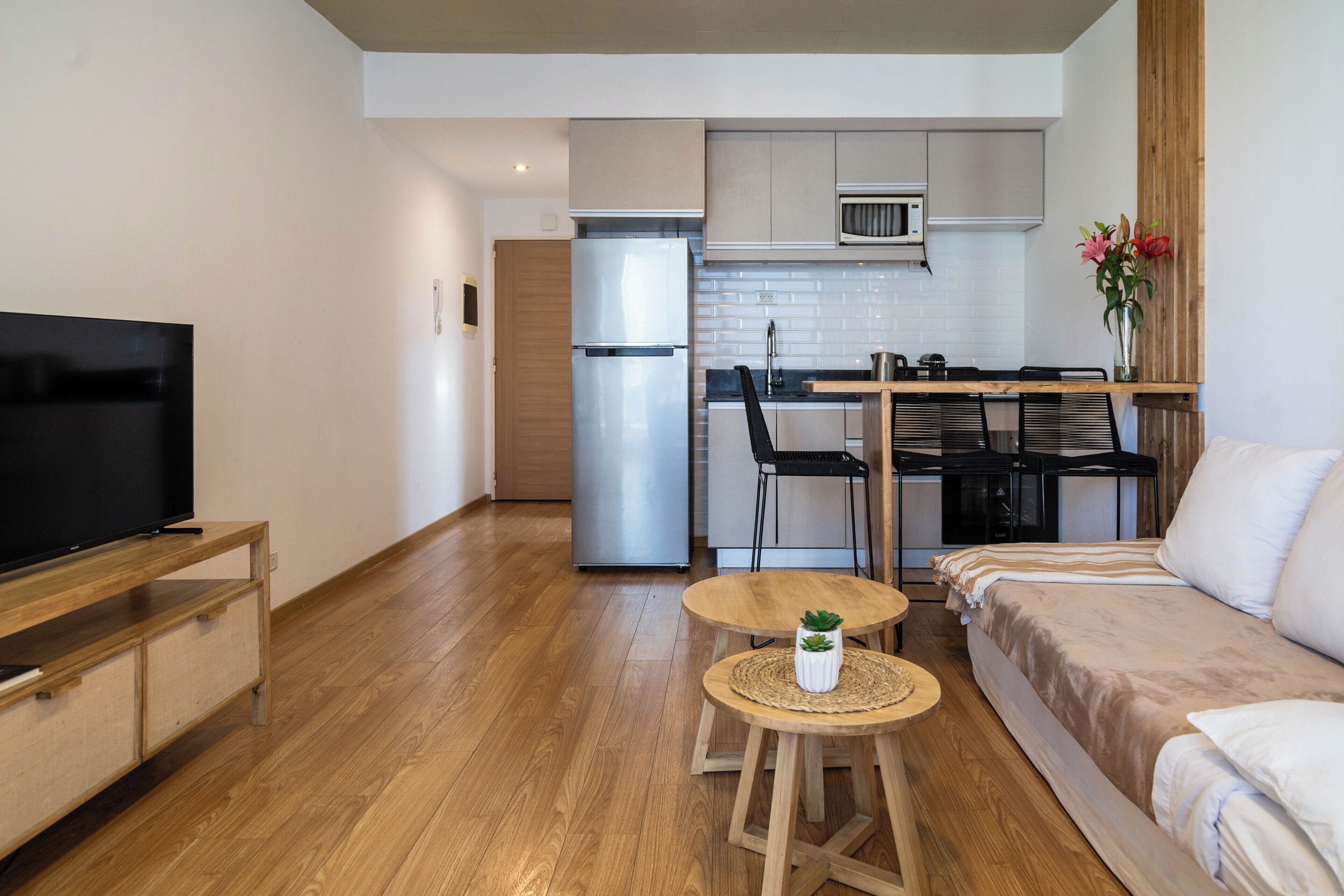 A compact living space with a kitchenette, a sofa, a TV, and a small table with a plant.