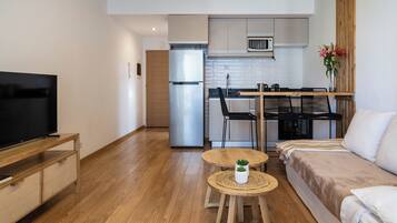 A compact living space with a kitchenette, a sofa, a TV, and a small table with a plant.