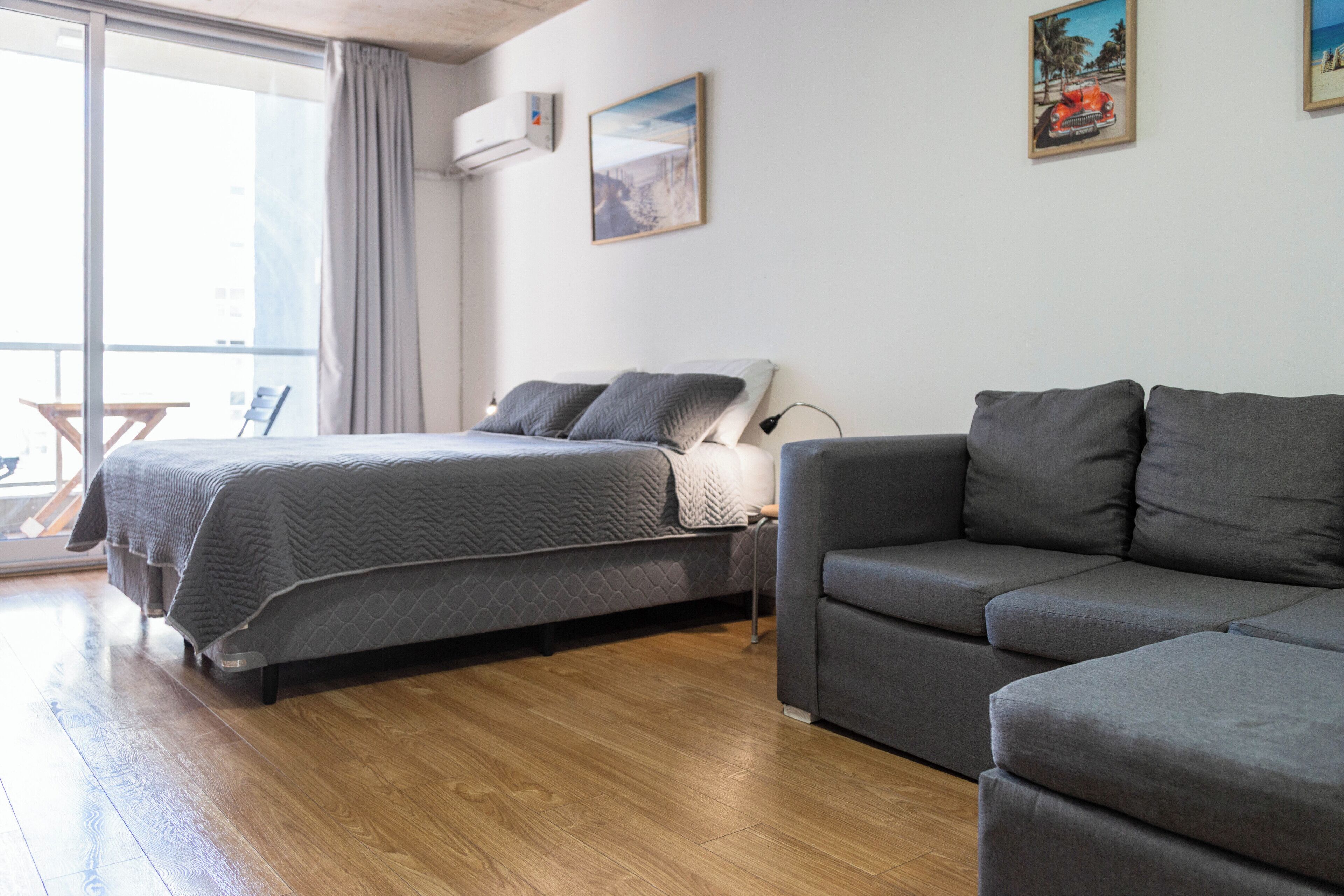A modern hotel room with a bed, a sofa, and a large window.