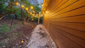 Ein Holzgebäude mit Kiesweg, der zu einer Tür führt, umgeben von Bäumen und Lichterketten.