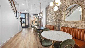 A modern dining area with a brick wall, round table, and green upholstered chairs. - BlueJay Hotel (Grand Rapids)