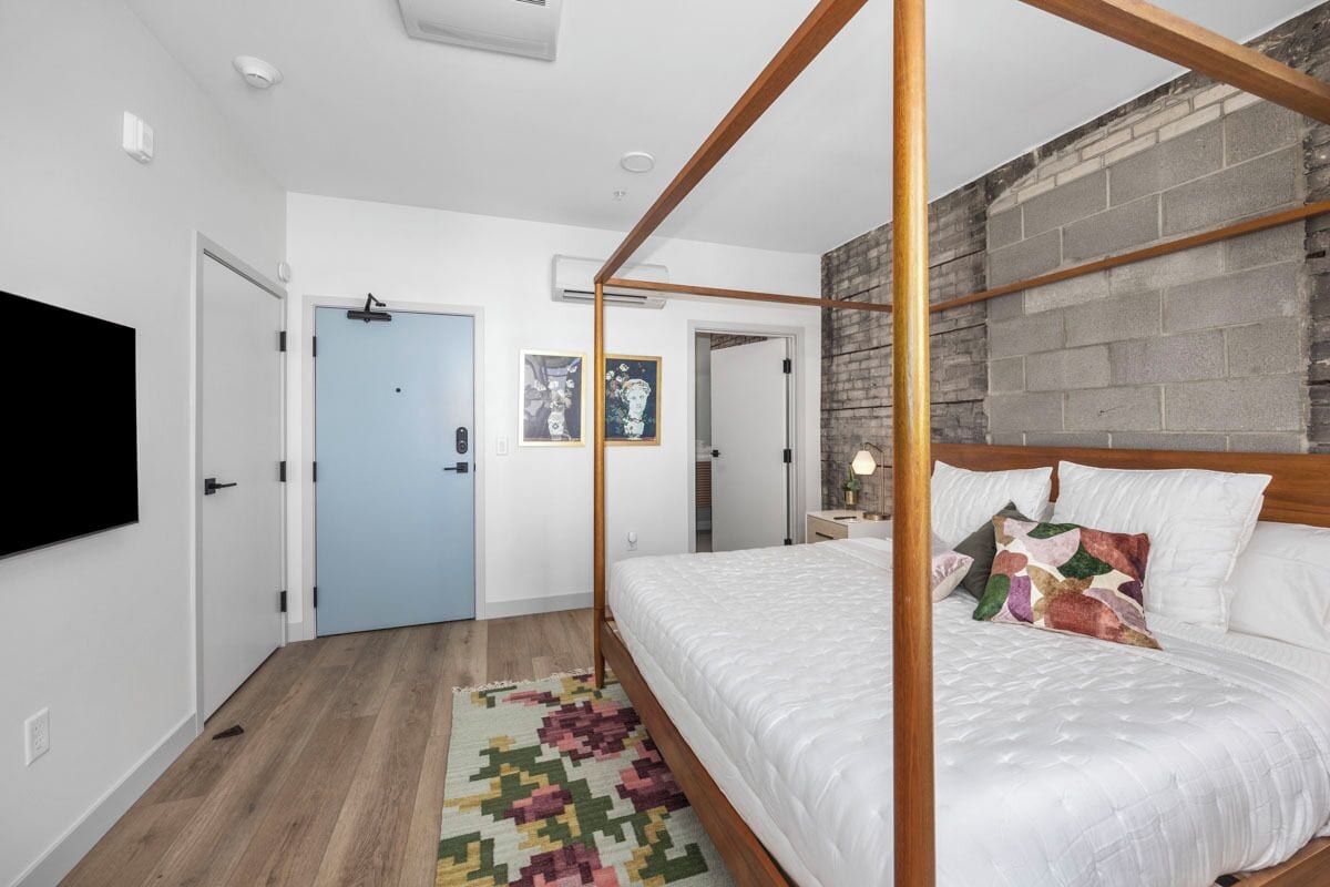 A modern bedroom with a four-poster bed, a wooden floor, and a brick accent wall.