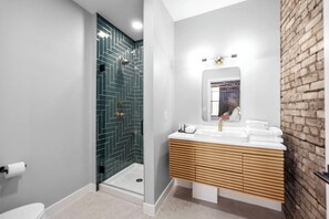 A modern bathroom with a shower, a sink with a wooden vanity, and a mirror. - BlueJay Hotel (Grand Rapids)