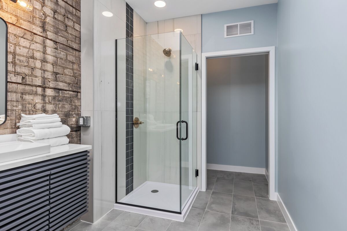 Un baño moderno con ducha de vidrio, tocador blanco con espejo y una pared decorativa de ladrillo.