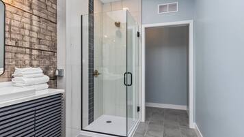 Un bagno moderno con cabina doccia in vetro, un mobile lavabo bianco con specchio e una parete in mattoni a contrasto.