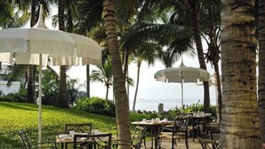 An outdoor dining area with tables and chairs, surrounded by palm trees and a view of the ocean.