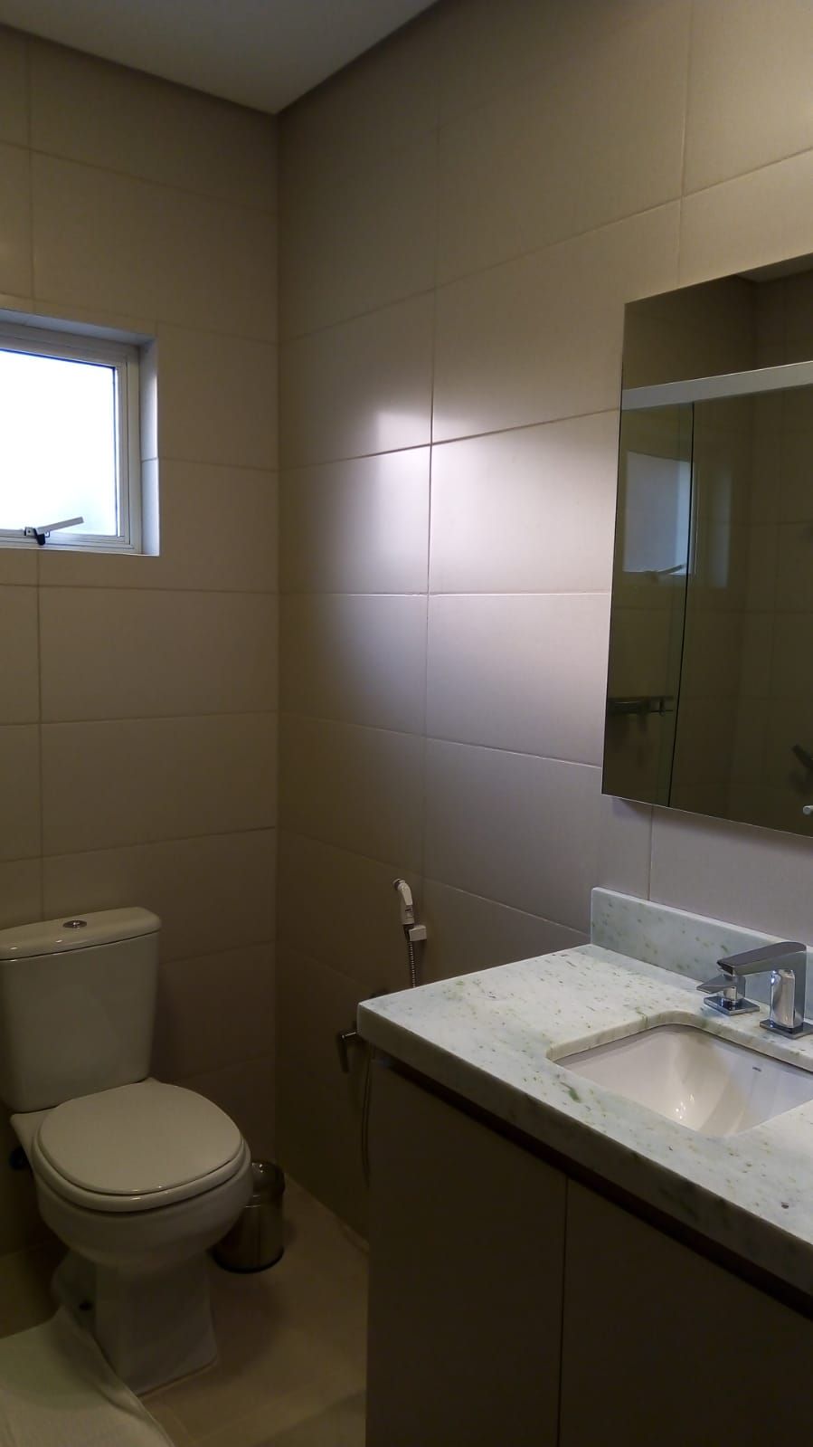 Ein kleines, sauberes Badezimmer mit Toilette, Waschbecken und Fenster.