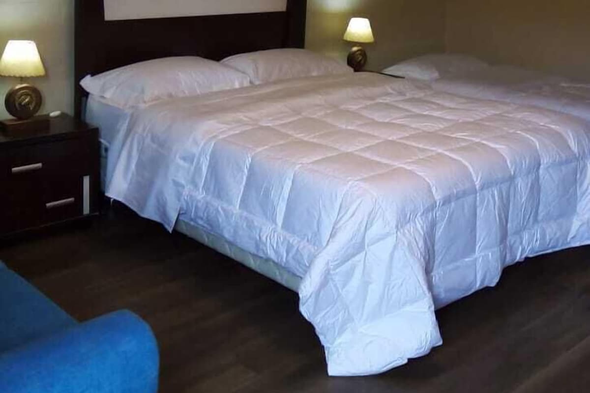 Un dormitorio con una cama grande, dos lámparas de noche, un cabecero de madera oscura y una silla azul.