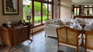 A spacious living room with large windows, a white sofa, a wooden cabinet, and a dining area with wicker chairs. - Haras Di Cellius (Bage)