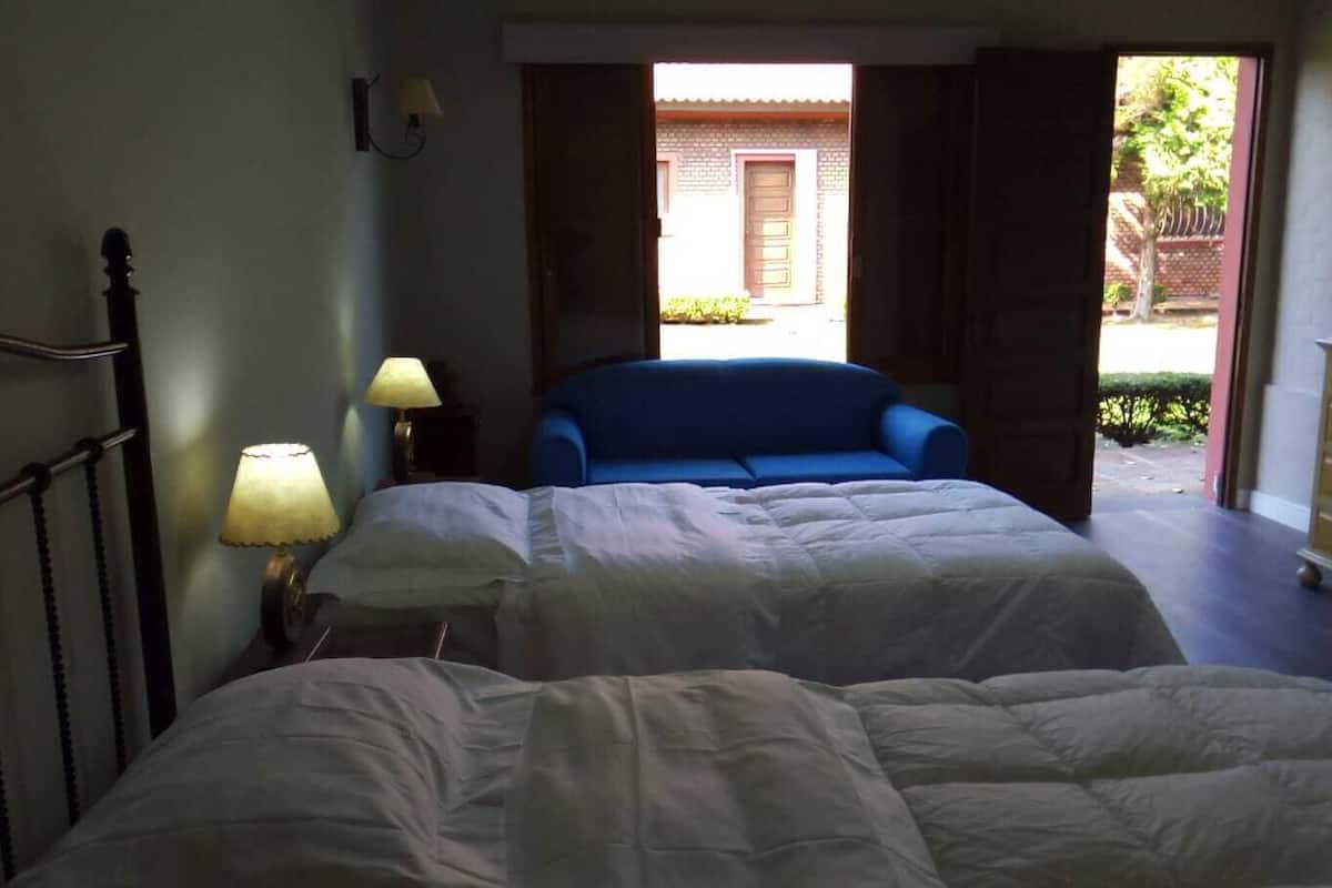 Quarto com duas camas, um sofá azul, cômoda e abajur.