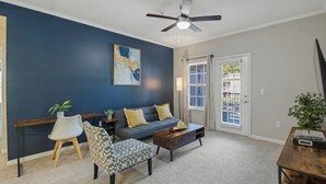 Ein Wohnzimmer mit dunkelblauer Akzentwand, Deckenventilator, einer gelb gepolsterten Couch, einem gemusterten Sessel und einem Couchtisch.