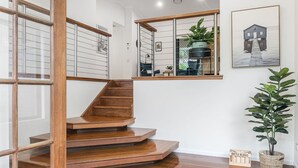 A wooden staircase leading to a second-floor landing with a glass railing, a potted plant, and a framed artwork on the wall. - Serenity Now - New Property, minutes from the beach and village, yet so peaceful and private (Lennox Head)
