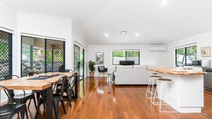 A modern kitchen with a wooden island, a dining area with chairs, and a living area with a sofa and a TV. - Serenity Now - New Property, minutes from the beach and village, yet so peaceful and private (Lennox Head)