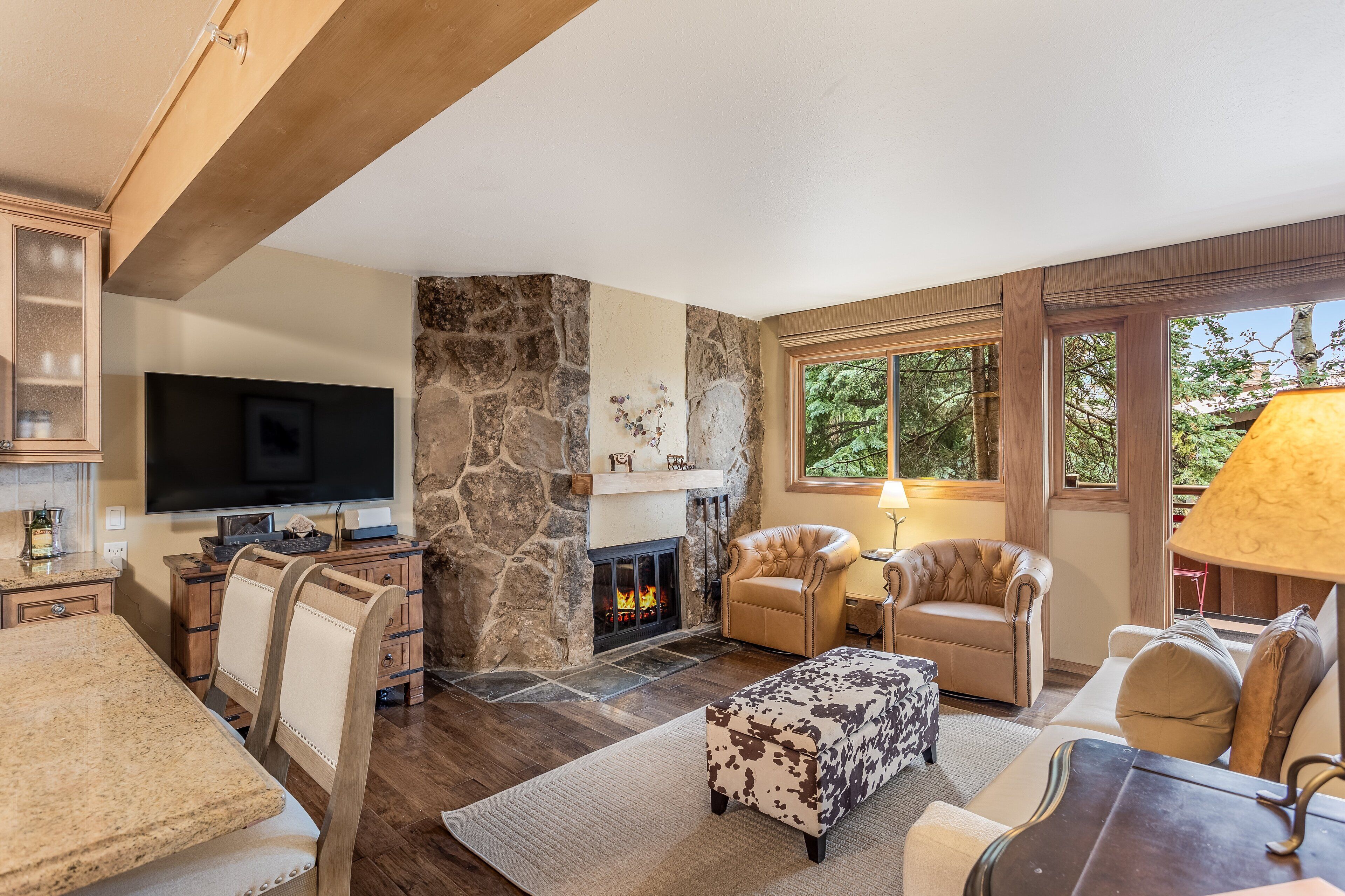 A living room with a stone fireplace, leather chairs, a TV, and a large window.