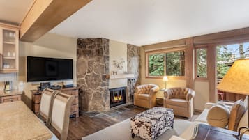 A living room with a stone fireplace, leather chairs, a TV, and a large window.