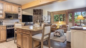 Una cocina con armarios de madera, una pared de acento de piedra, una isla grande y un comedor con sillas de cuero y una mesa.