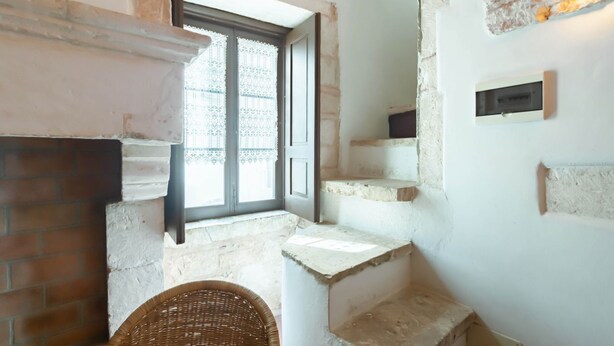 Un escalier avec un mur en briques, une chaise en osier et une fenêtre ornée de rideaux en dentelle.