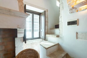 A staircase with a brick wall, a wicker chair, and a window with lace curtains.