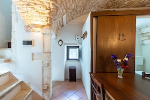 A room with a stone ceiling, a wooden door with a toilet sign, a small window, and a vase with flowers on a table.