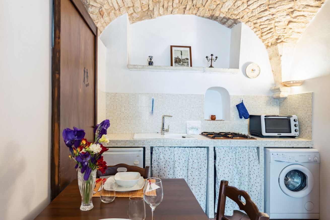 A kitchen with a stone arch, a sink, a microwave, and a washing machine.