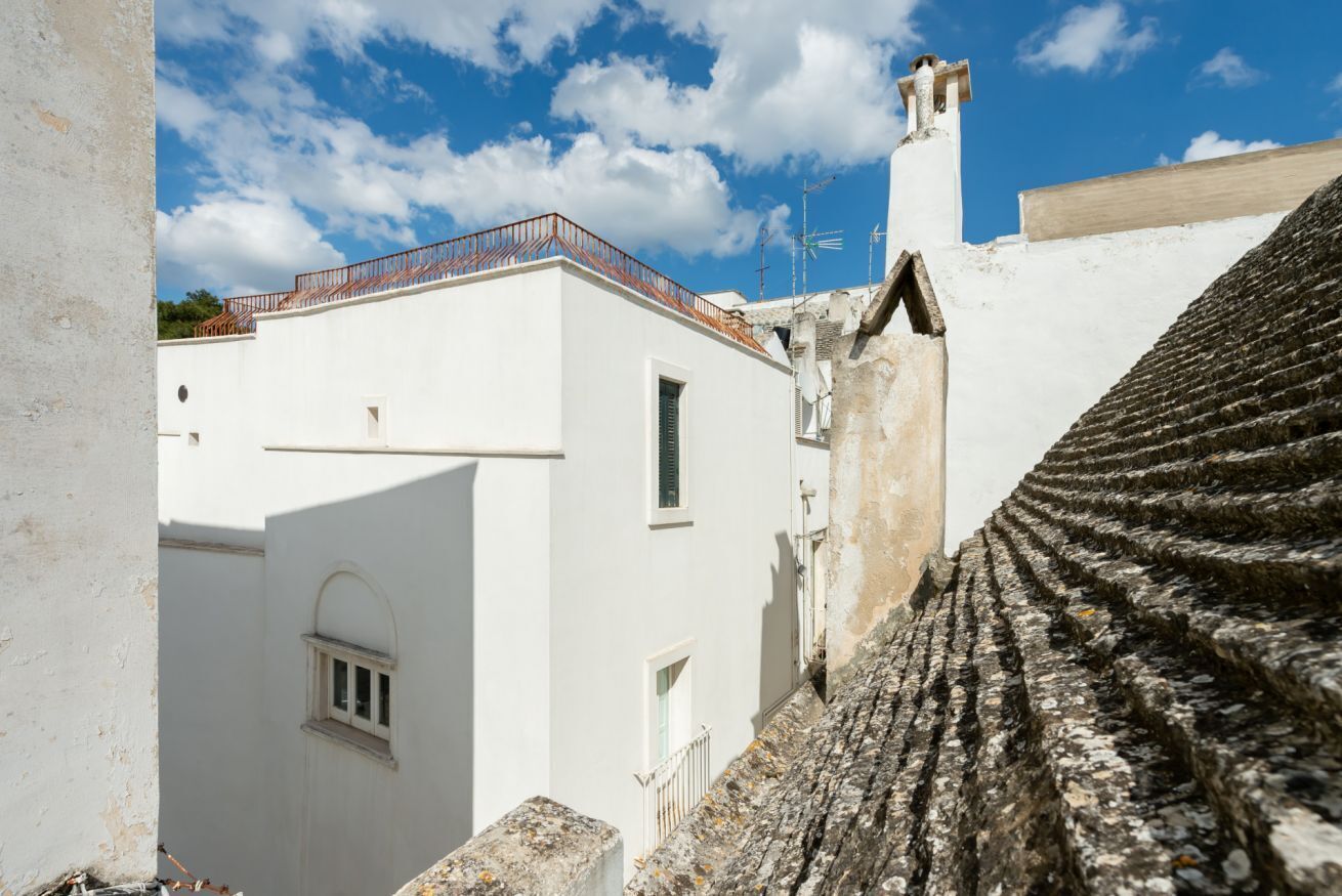 Un bâtiment blanc avec un toit recouvert de tuiles, une petite fenêtre et un garde-corps en métal.