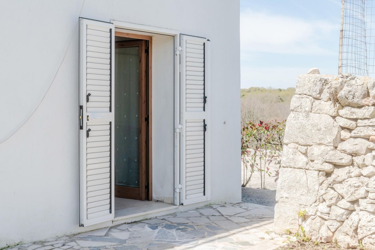 A white building with a stone wall and a door with shutters.