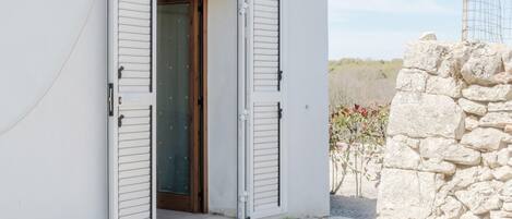 A white building with a stone wall and a door with shutters.